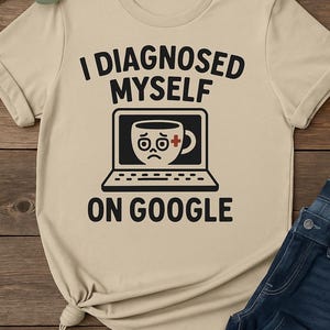 May include: Beige t-shirt with the text "I DIAGNOSED MYSELF ON GOOGLE". The graphic shows a laptop with a sad-faced coffee cup and a red cross symbol. The shirt is paired with blue jeans.