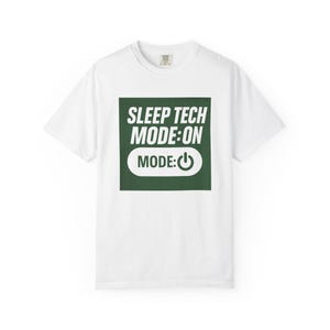 May include: White t-shirt with a green square graphic. The graphic reads "SLEEP TECH MODE: ON" above "MODE:" and a power button symbol. The shirt is a crew neck style.