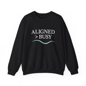 May include: Black crew neck sweatshirt with the text "ALIGNED > BUSY" in white, above a light teal wavy line. The sweatshirt is a solid black color and has long sleeves.
