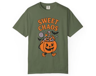 May include: An olive green t-shirt with the words "SWEET CHAOS" in orange. The design features a cartoon jack-o'-lantern filled with sweets and bats. The t-shirt is short-sleeved and has a crew neck.