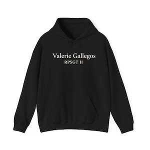 Può includere: Felpa con cappuccio nera con tasca frontale e coulisse. Il testo "Valerie Gallegos RPSGT II" è stampato in bianco sul petto. Un capo casual e confortevole.