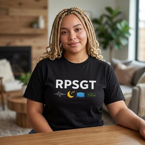 Peut inclure: T-shirt noir avec le texte blanc "RPSGT" au-dessus d'une ligne de battement de cœur, d'un croissant de lune avec "zzz", d'un oreiller bleu et d'une horloge numérique indiquant 3h00. Le t-shirt est porté par une personne aux tresses blondes.