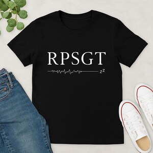 以下が含まれることがあります： 「RPSGT」という白い文字と、その下に「zz」という文字が書かれたスタイリッシュな心拍数グラフが描かれた黒いTシャツです。