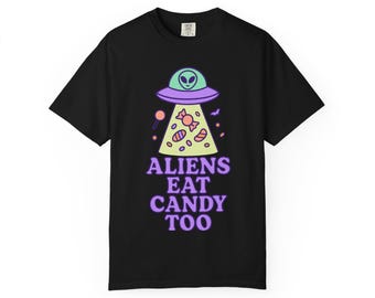 May include: Black t-shirt with a colorful graphic of a UFO, an alien, and candy. The text "ALIENS EAT CANDY TOO" is in purple. The design is centered on the front of the shirt.