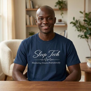 Könnte beinhalten: Ein marineblaues T-Shirt mit dem Text "Sleep Tech" in weißer Schrift, über einem weißen Wellenform-Design und den Worten "Monitoring Dreams Professionally". Ein Mann trägt das T-Shirt und lächelt in die Kamera.