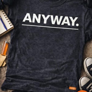 Pode incluir: Camiseta cinza escuro com a palavra "ANYWAY." em branco, sublinhada. A imagem inclui um caderno, fones de ouvido, um isqueiro, um controle de jogo e tênis. O texto "READY TO DOWNLOAD ANYWAY. PNG & SVG" também é visível.