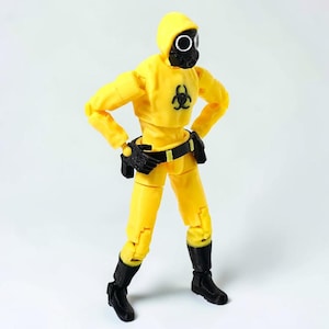 May include: A yellow hazmat suit action figure with a black gas mask and hood. The figure features a black biohazard symbol on the chest, a black utility belt with a holster, and black boots. The articulated figure stands in a pose with hands on hips.