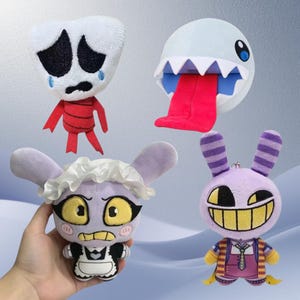 Puede incluir: Una colección de cuatro peluches que incluye un personaje blanco llorando con extremidades rojas, una criatura redonda azul claro con dientes afilados y una lengua roja larga, un personaje morado con traje de sirvienta y un conejo morado con una sonrisa.