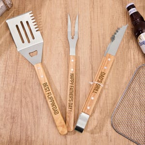 Può includere: Un set di tre utensili da barbecue con manici in legno e teste in acciaio inossidabile. Il set include una spatola con "BEST FLIPPIN' DAD" inciso, una forchetta con "HAPPY FATHER'S DAY!" e pinze con "DAD'S GRILL".
