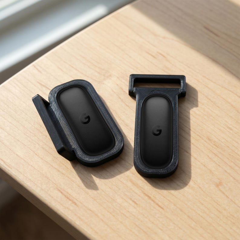 May include: Two black plastic mounts with textured surfaces, each holding a black oval-shaped device featuring a small letter G logo in the center. One mount is angled with a side bracket, while the other is flat with a rectangular top loop.