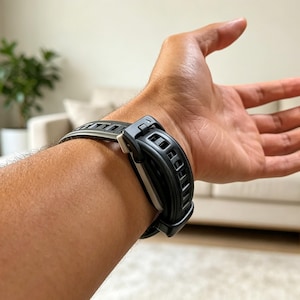 May include: A black watch strap featuring a textured, vented design with a secure buckle mechanism. The strap is constructed from a flexible material and includes a silver-toned metal connector piece that attaches the band to the watch casing.