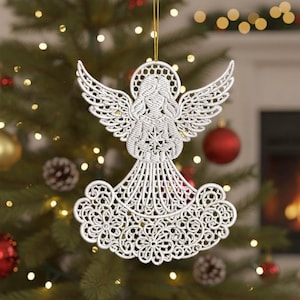 Puede incluir: Adorno navideño de ángel blanco con un diseño intrincado. El ángel tiene alas detalladas, un halo y un vestido fluido. El adorno está suspendido por un hilo dorado, sobre un fondo borroso de árbol de Navidad.