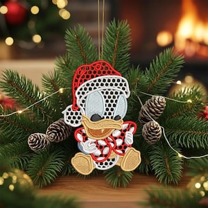 Puede incluir: Adorno navideño bordado con un pato de dibujos animados que lleva un gorro de Papá Noel y un atuendo con estampado rojo y blanco. El adorno cuelga frente a un árbol de Navidad con piñas y luces. El adorno está hecho de hilo rojo, blanco, negro y beige.