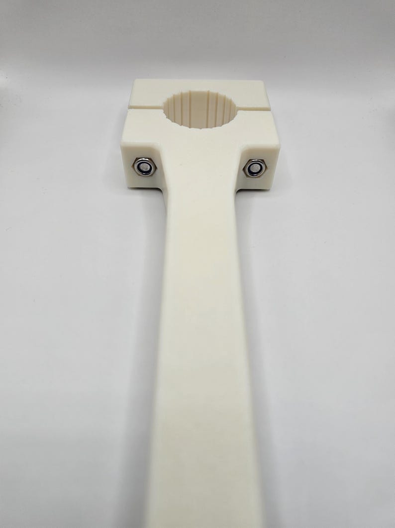 May include: A cream-colored, T-shaped clamp with a circular opening and a long handle. Two bolts secure the clamp's top section. The object is made of a smooth, solid material and is set against a plain white background.