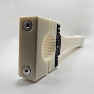May include: A cream-colored, rectangular object with a cylindrical opening and a handle. Two silver screws secure the object's front. The text "MADE IN USA" is printed in black on the side. The object is likely a tool or a fixture.