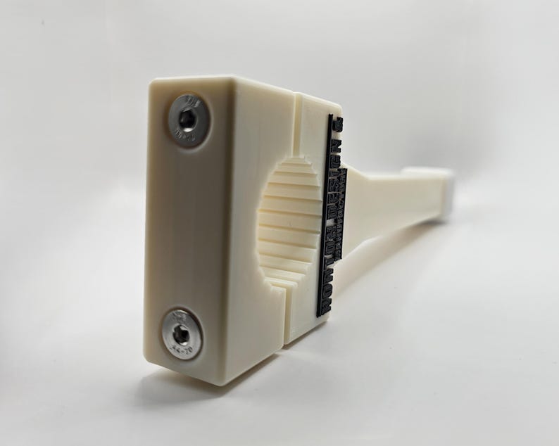May include: A cream-colored, rectangular object with a cylindrical opening and a handle. Two silver screws secure the object's front. The text "MADE IN USA" is printed in black on the side. The object is likely a tool or a fixture.