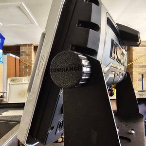 Könnte beinhalten: Ein schwarzer Lowrance-Fischfinder, der auf einem Boot mit einem schwarzen Gummiknopf montiert ist. Der Fischfinder hat ein silber-schwarzes Design.