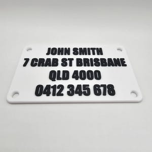 May include: White plastic nameplate with black text. The text reads "JOHN SMITH", "7 CRAB ST BRISBANE", "QLD 4000", and "0412 345 678".