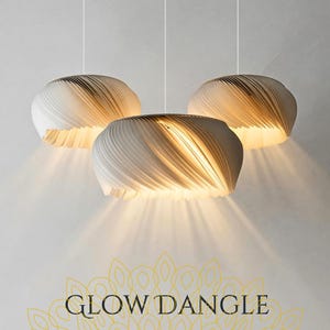 Könnte beinhalten: Drei weiße, spiralförmige Pendelleuchten mit warmem Schein. Die Leuchten hängen von der Decke und werfen das Licht nach unten. Der Text "GLOW DANGLE" ist unten im Bild zu sehen.