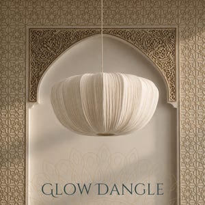 May include: A cream-colored, round, pleated fabric pendant light fixture suspended by a thin cord. The shade features a soft, textured, ribbed surface with a wide, flattened, circular shape. The text GLOW DANGLE is printed in dark blue at the bottom.