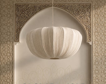 May include: A cream-colored, round, pleated fabric pendant light fixture suspended by a thin cord. The shade features a soft, textured, ribbed surface with a wide, flattened, circular shape. The text GLOW DANGLE is printed in dark blue at the bottom.