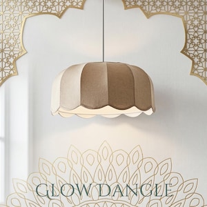 May include: A beige and cream-colored pendant light with a scalloped edge. The light fixture is suspended from a black cord against a white wall with gold decorative accents. The text "GLOW DANGLE" is at the bottom.