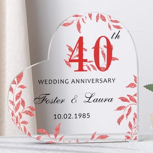 Könnte beinhalten: Ein herzförmiges Hochzeitsjubiläum-Andenken aus Acryl. Das klare Acryl hat rote florale Akzente und den Text "40. Hochzeitstag" mit den Namen "Foster & Laura" und dem Datum "10.02.1985".