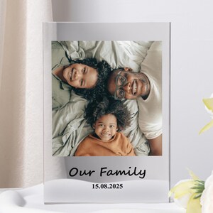 May include: A clear acrylic photo frame displaying a family portrait. The photo features a smiling family of three. The text "Our Family" and the date "15.08.2025" are printed at the bottom of the frame.