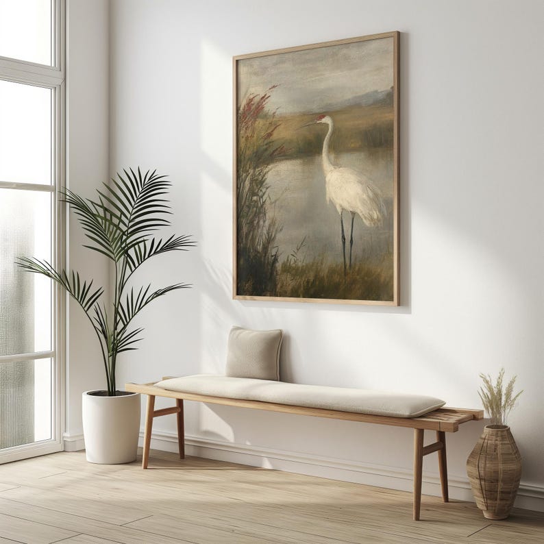 May include: A framed painting depicting a white crane standing in a marsh with reeds and water. The painting features a muted colour palette of browns, greens, and greys.
