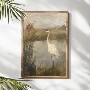 May include: A vintage painting depicting a white crane standing in a marsh with tall reeds. The crane has a long neck and long legs. The background is a soft, muted green and brown.