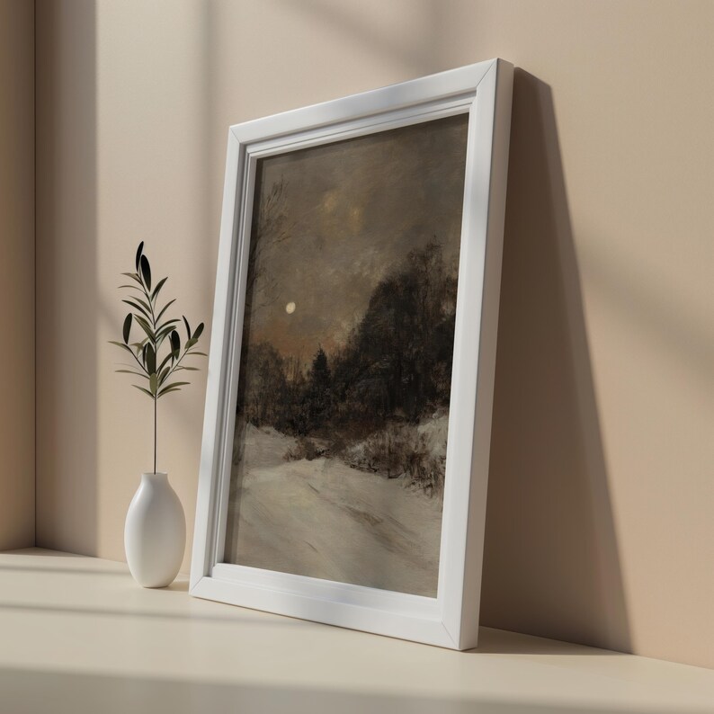 May include: A framed painting of a snowy landscape with a full moon in the sky. The painting is in a white frame and is hanging on a wall.
