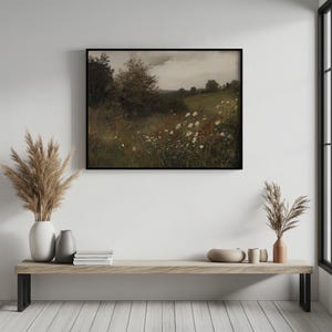 May include: A framed landscape painting depicts a field of wildflowers under a cloudy sky. The artwork features a meadow with white and red flowers, green grass, and trees. The painting is displayed above a wooden bench with decorative vases and books.