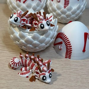 May include: White and red baseball-themed figurines. One figurine is a baseball-themed creature with brown appendages. Other figurines are baseball-themed eggs with baseball stitching and a baseball bat accent. The figurines are on a light brown surface.