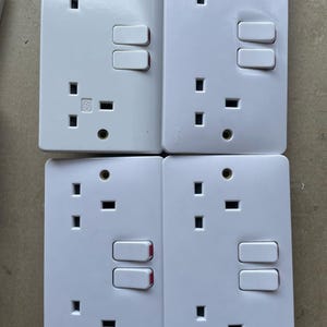 May include: Four white electrical outlet covers with two toggle switches each. The switches have red indicator lights. The outlets are standard three-pin plugs.
