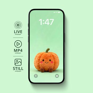 May include: A smartphone displays a cute, plush orange pumpkin with a smiling face on a light green background. The time 1:47 is displayed at the top. The phone is black with a green background.