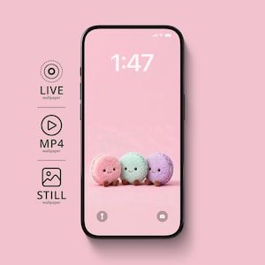May include: A smartphone displays a pink wallpaper with three plush macarons in pink, mint green, and purple. The time 1:47 is shown at the top. The phone is set against a pink background, with icons for live, MP4, and still wallpapers.