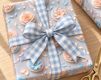 Può includere: Una scatola regalo rettangolare avvolta in carta azzurra con un motivo di cupcake floreali rosa e blu e nastri, legata con un fiocco di nastro a quadretti blu e bianco, accompagnata da un rotolo di carta abbinata e forbici dorate.