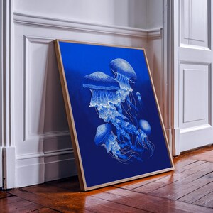 May include: A framed art print featuring a detailed illustration of several jellyfish in shades of blue and white against a deep blue background. The artwork is displayed in a natural wood frame, leaning against a white wall.