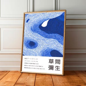 Puede incluir: Un cuadro enmarcado con un diseño abstracto azul y blanco. La obra de arte, en un marco de madera, está apoyada contra una pared blanca y un suelo de madera. Texto japonés visible en la parte inferior derecha.