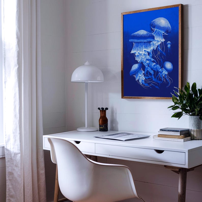 May include: A framed art print featuring a cluster of blue jellyfish against a deep blue background. The artwork is displayed in a room with a white desk, chair, and lamp. A small plant and decorative items are also on the desk.