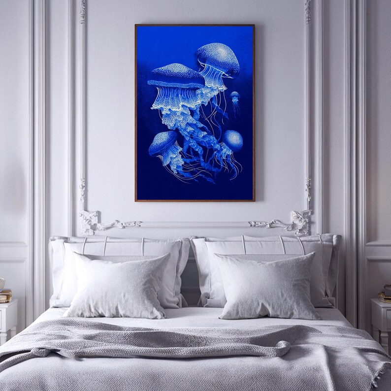 May include: A framed art print featuring a detailed illustration of several blue jellyfish against a deep blue background. The jellyfish have intricate white detailing, creating a striking contrast. The artwork is displayed above a bed with white pillows and a gray blanket.