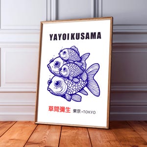 May include: A framed art print with a blue illustration of three fish. The print includes the name "YAYOI KUSAMA" in black text at the top and Japanese text at the bottom, with "TOKYO" in English. The artwork is displayed on a wooden floor.
