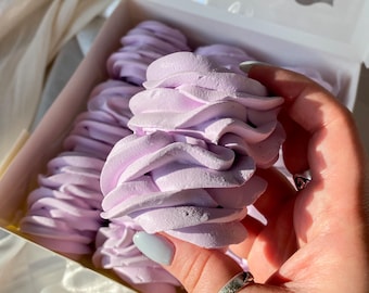 May include: A box of lavender-colored, swirled marshmallows. The marshmallows are in a white box with a clear window. The image is taken in natural light, highlighting the soft texture and color of the treats.