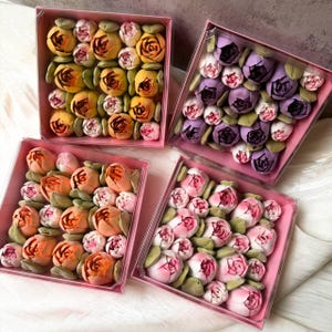Pu&ograve; includere: Quattro scatole quadrate rosa riempite di dolciumi a forma di fiore. Ogni scatola contiene una collezione di piccoli fiori dettagliati nelle tonalit&agrave; del giallo, arancione, viola e rosa, intervallati da piccole foglie verdi nelle composizioni.