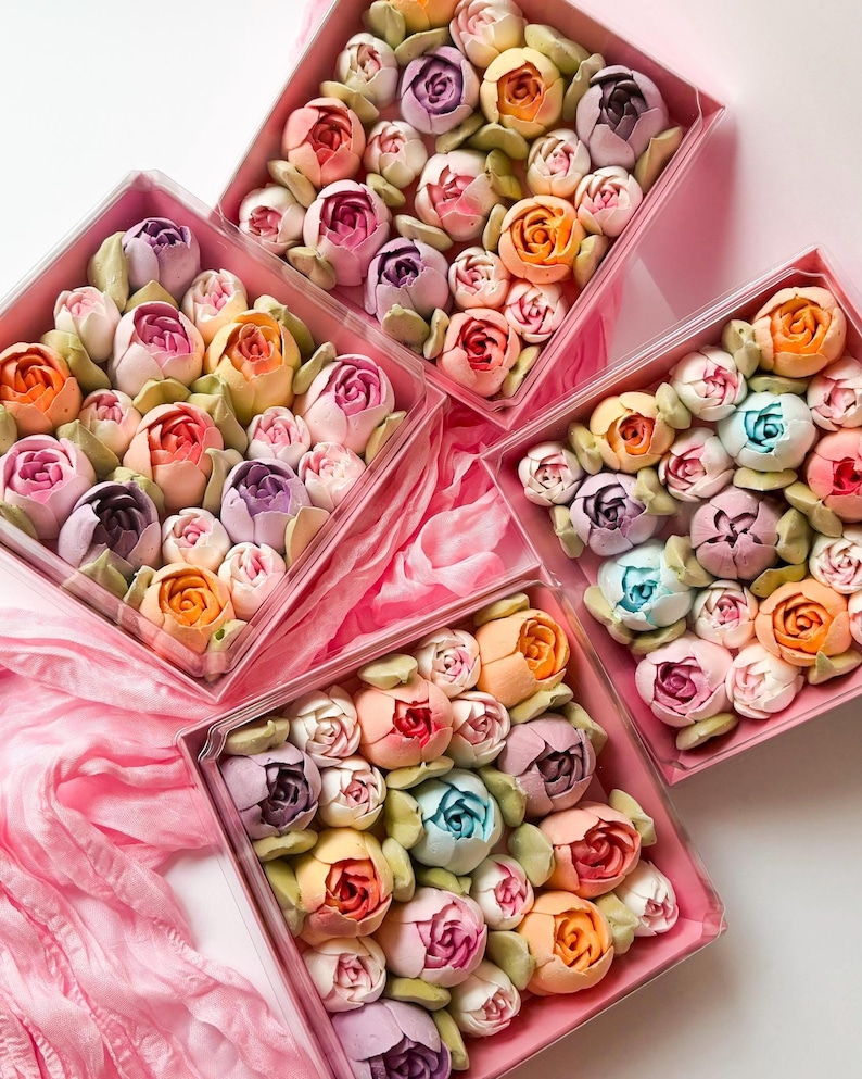 Pu&ograve; includere: Quattro scatole quadrate in plastica trasparente riempite con un assortimento di dolciumi multicolori a forma di fiore. I dolcetti sono disposti in grappoli compatti, con sfumature di rosa, viola, arancione, giallo e blu, accentuati da foglie verdi.