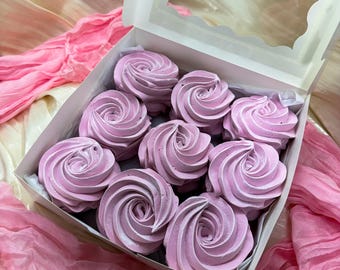 May include: A white box with a clear lid, filled with nine light purple, swirled marshmallows. The marshmallows have a rose-like design. Pink fabric is visible in the background.
