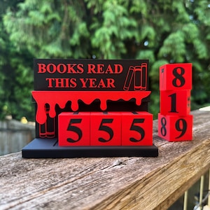 May include: A black and red wooden book tracker with the text "BOOKS READ THIS YEAR." The tracker has red number blocks to display the number of books read. The current number displayed is 555.