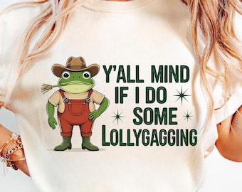 May include: Cream-colored t-shirt featuring a cartoon frog wearing a cowboy hat and overalls, with a straw in its mouth. The text reads "Y'ALL MIND IF I DO SOME LOLLYGAGGING" in green. The frog is green, the overalls are red.