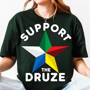 Può includere: T-shirt verde scuro con le parole bianche "SUPPORT THE DRUZE". Al centro c'è una stella multicolore, con punte verdi, rosse, gialle, blu e bianche. La maglietta è realizzata in materiale morbido.