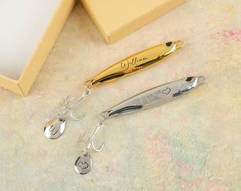 Könnte beinhalten: Zwei Angelköder, einer goldfarben und einer silberfarben, mit Haken und personalisierten Details. Der goldfarbene Köder trägt den eingravierten Namen "William". Der silberfarbene Köder hat den Text "I LOVE YOU MORE THAN I LOVE FISHING" und ein Herzsymbol.